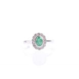 An emerald and diamond cluster ring, the oval cut emerald within a border of eight cut diamonds to a