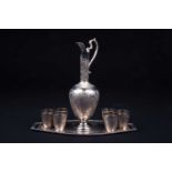 An Eastern white metal ewer, with six conforming tots and shaped oval tray, each with finely