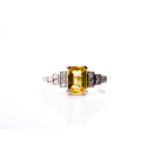 A platinum, diamond, and yellow sapphire ring set with a mixed emerald-cut yellow sapphire of