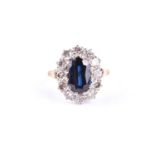 A sapphire and diamond cluster ring, the large oval mixed cut sapphire, claw mounted within a border
