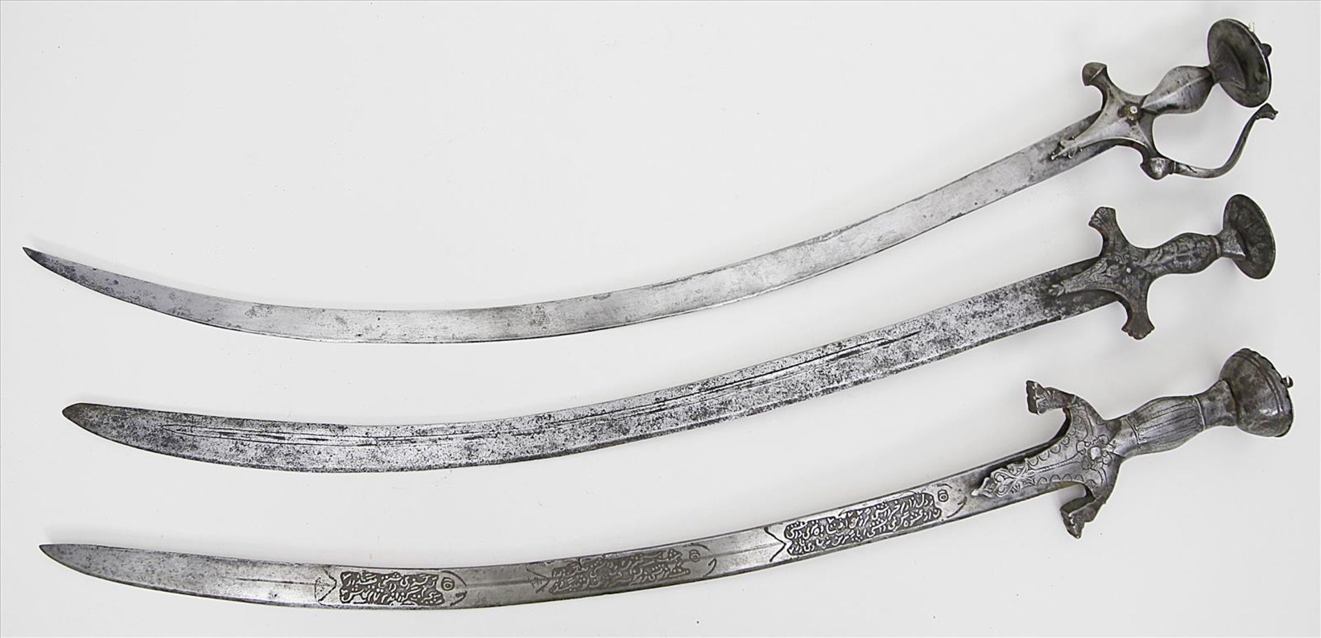 Drei Tulwar-Schwerter.Gebogte Eisenklingen, einmal mit arabischer Inschrift. Eisengriff. Alters- und