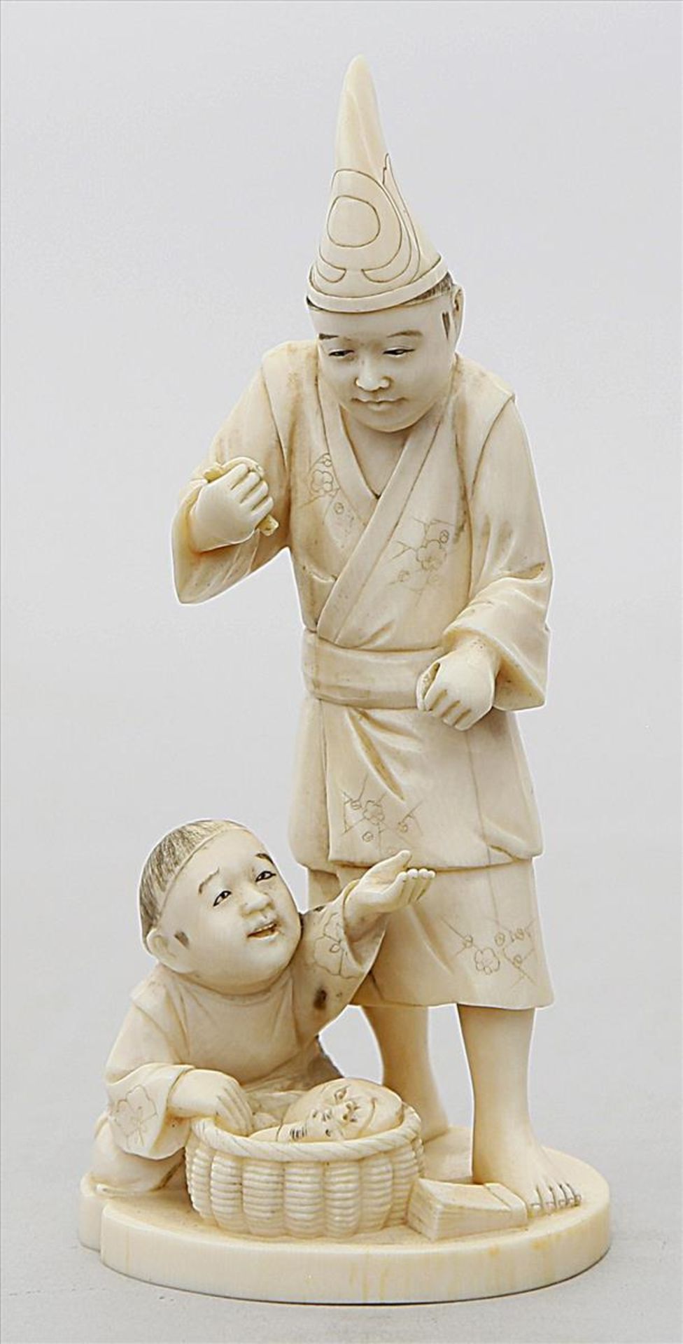 Okimono.Elfenbein, geschnitzt, Boden mit eingelegter Siegelplatte. Mann mit Junge und Korb voller