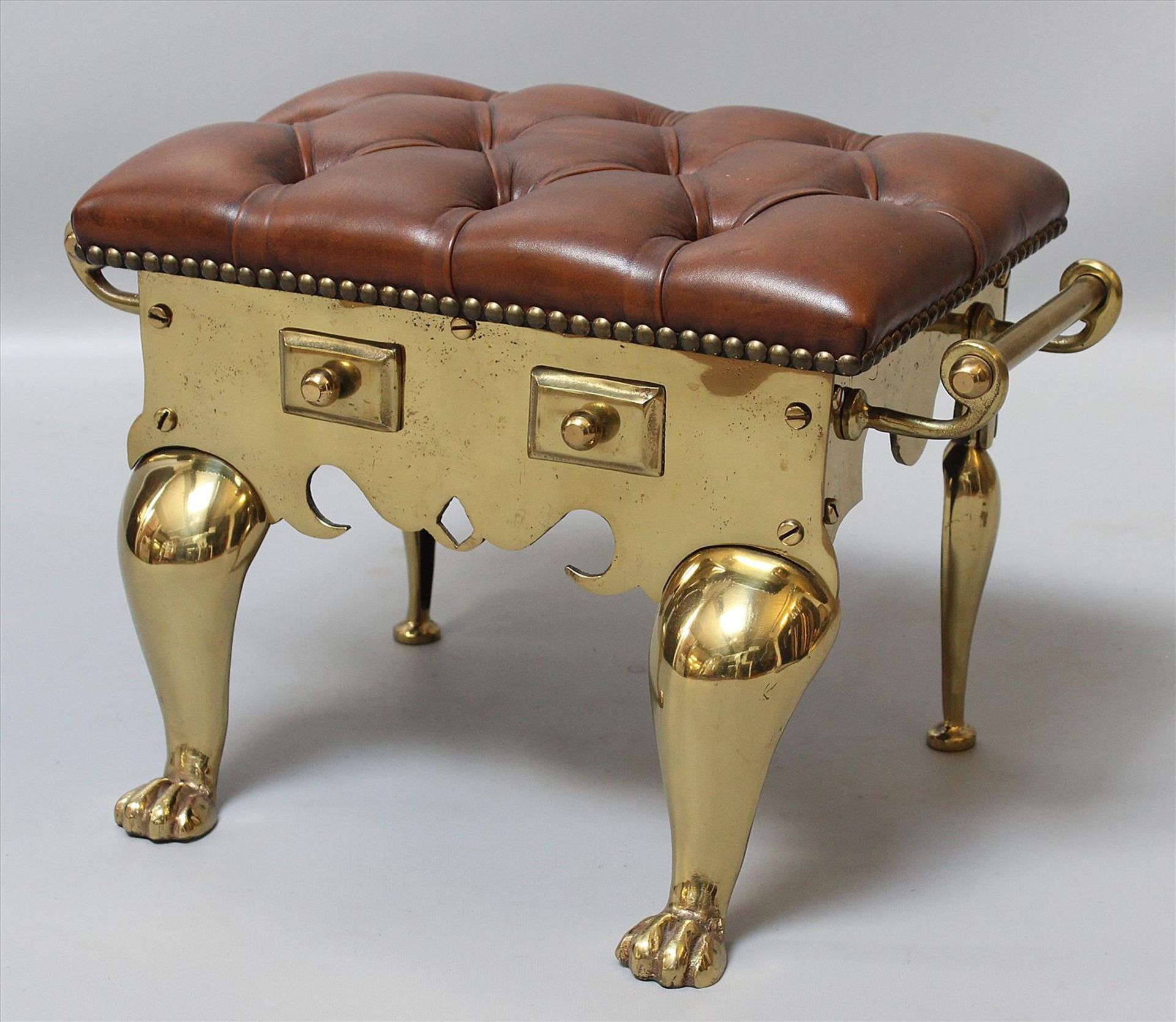 Hocker.Schweres Messinggestell mit seitlichen Griffen. Braune "Chesterfield"-Polsterung.