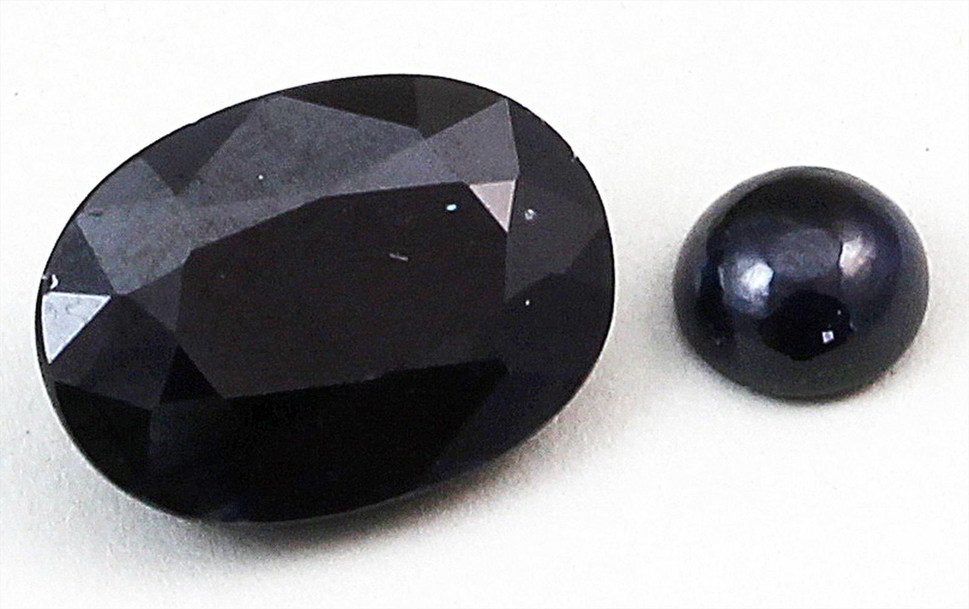 2 dunkelblaue Saphire, zus. ca. 7,9 ct.Je einmal oval facettiert bzw. rundes Cabochon.