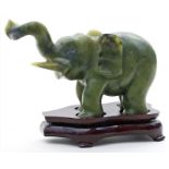 Stehender Elefant mit erhobenem Rüssel.Jadefarbener Steatit. China.H. 8 cm. Beigegeben: Holzsockel.