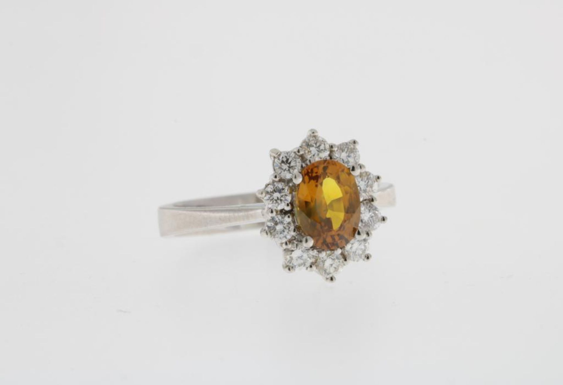 Een witgouden entourage bezet met een oranje saffier, ca. 1,13 ct, en briljant geslepen diamanten,