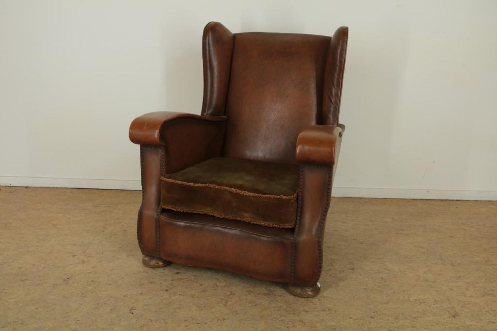 Bruinlederen Art Deco heren oorfauteuil met groen velourse kussen.