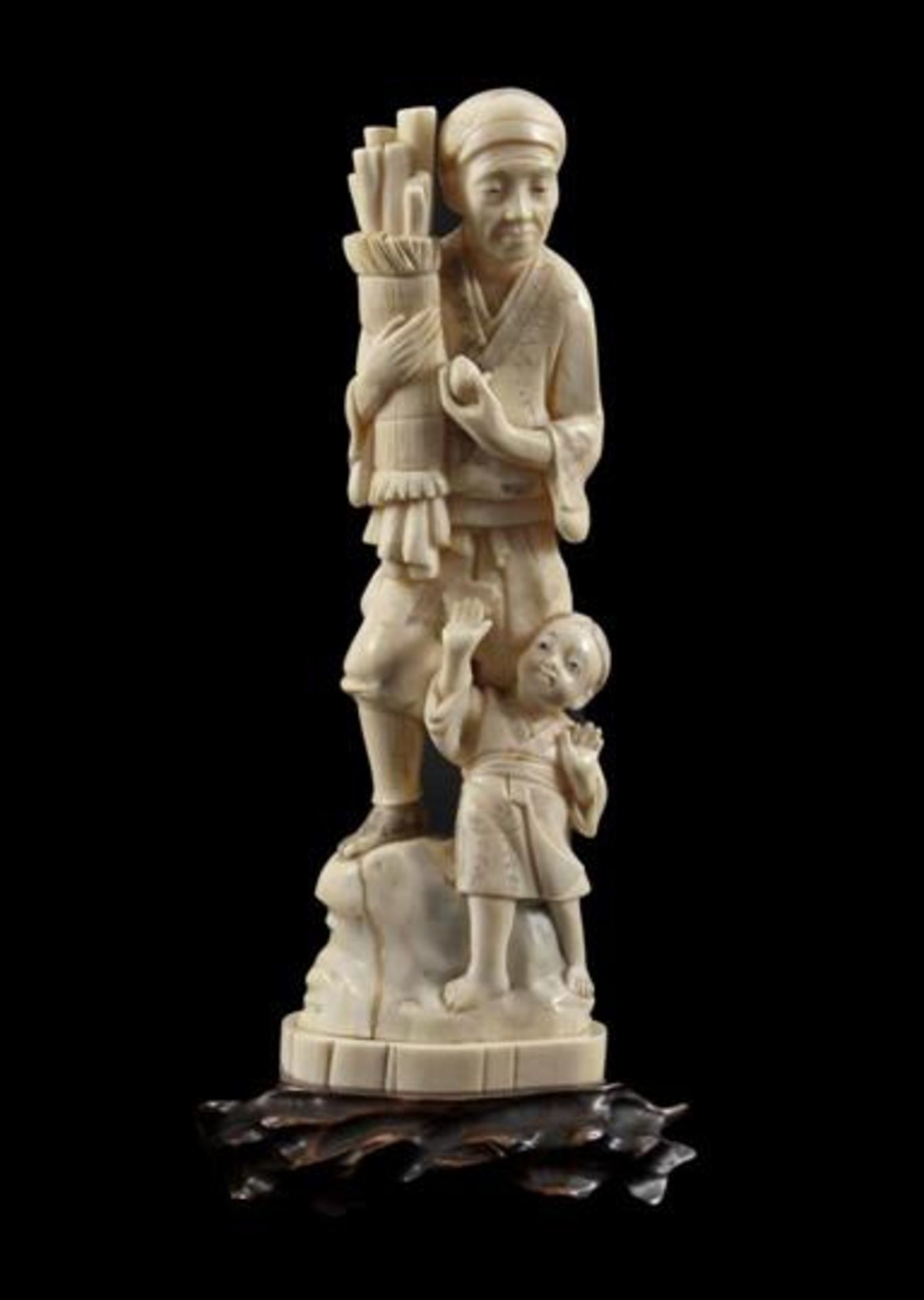 Ivory carved sculpture of a man with child on a rock with a pack of branches in his hand, Japan,