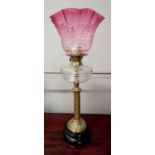 A 19th century Corinthian column oil lamp having a cranberry glass shade above stylized thistle