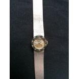 A Bueche Girod Lady~s 9ct white gold wrist watch having a diamond and emerald surround to face.