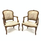 Pair of French style walnut salon elbow chairs, floral carved cresting rail,