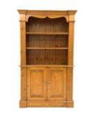 20th century varnished pine bookcase on cupboard, projecting cornice over shaped apron,