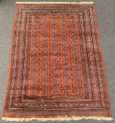 Persian design Bokhara ground carpet, repeating gul motif on burnt orange field, guarded border,