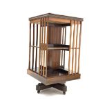 20th century mahogany revolving bookcase of two tiers, cruciform base, ceramic castors,