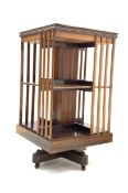 20th century mahogany revolving bookcase of two tiers, cruciform base, ceramic castors,