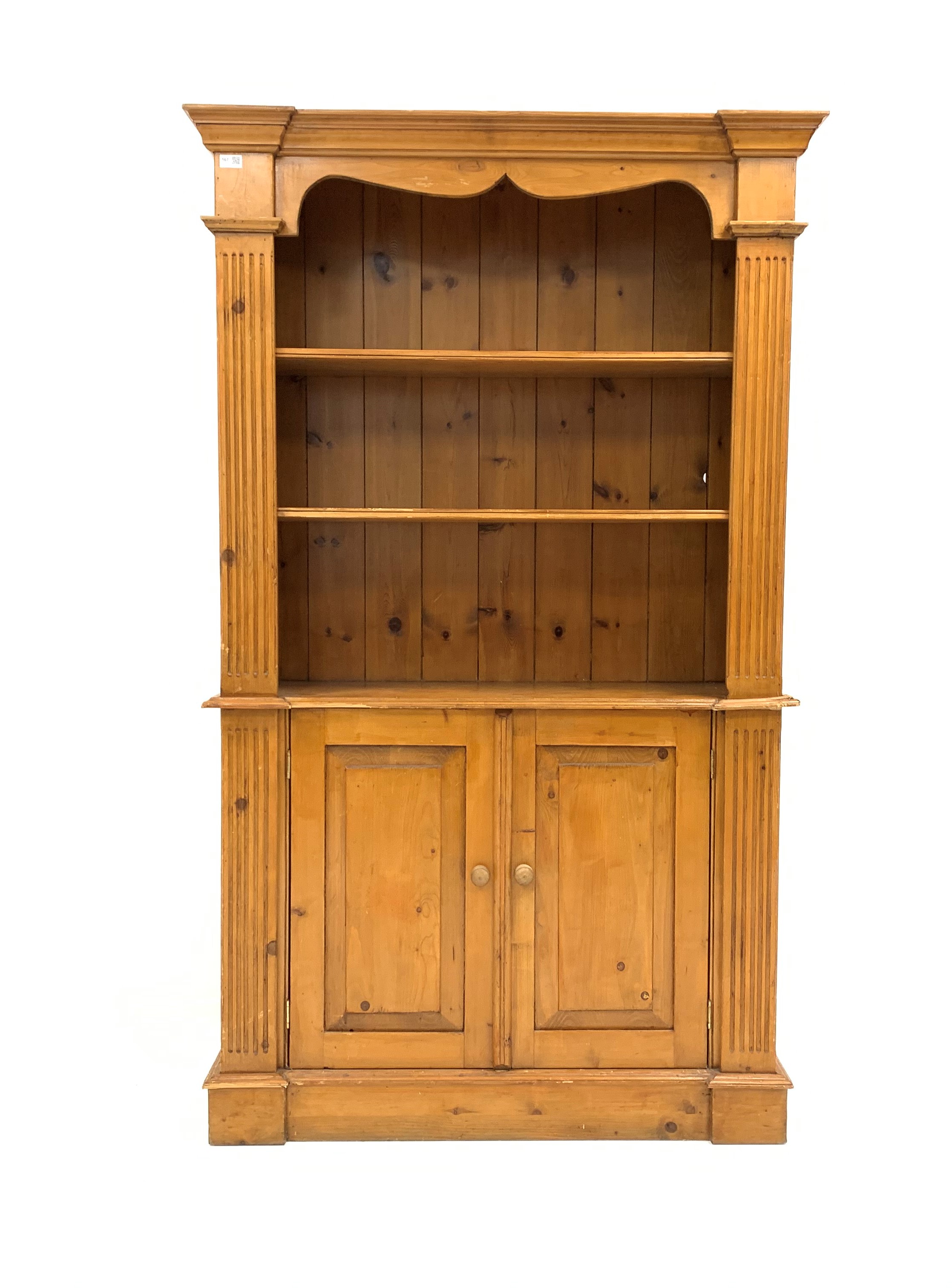 Edwardian varnished pine bookcase on cupboard, projecting cornice over shaped apron,