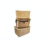 Three large wicker laundry baskets, the smallest having metal fittings and rope handles,