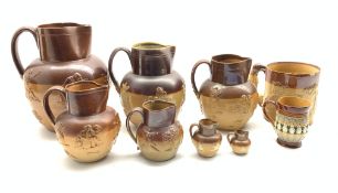 Group of six Doulton Lambeth stoneware harvest jugs, the two smallest with silver rims,