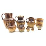 Group of six Doulton Lambeth stoneware harvest jugs, the two smallest with silver rims,