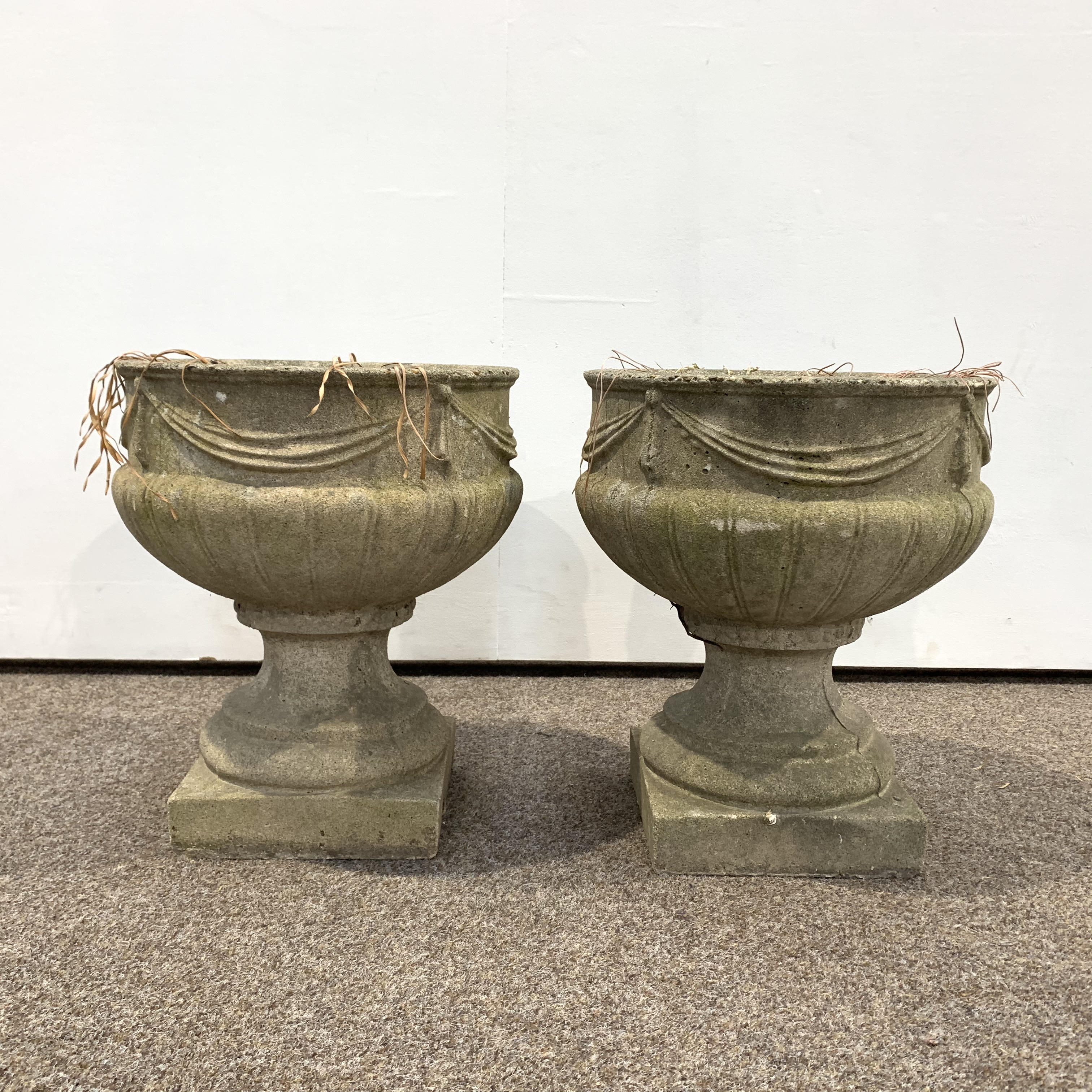 Pair of reconstituted stone garden urns decorated with ribbon swags and with lobe moulded bases,