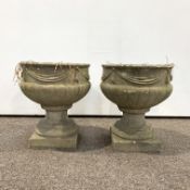 Pair of reconstituted stone garden urns decorated with ribbon swags and with lobe moulded bases,