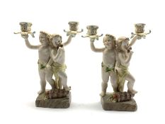 Two 20th century Continental porcelain two branch candelabra modelled as two cherubs playing pan pi