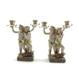 Two 20th century Continental porcelain two branch candelabra modelled as two cherubs playing pan pi