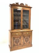 Edwardian walnut bookcase on cupboard, floral carved cornice over glazed doors enclosing three adju