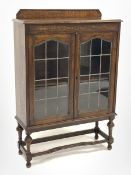 Early 20th century oak display cabinet, carved frieze over two lead glazed doors, turned supports co