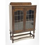 Early 20th century oak display cabinet, carved frieze over two lead glazed doors, turned supports co