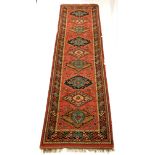 Red ground woollen runner rug, with lozenge and geometric design enclosed by multi line border, 340c
