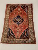 Persian red ground rug, with lozenge medallion on field decorated with stylised geometric floral des