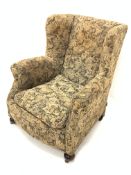 Victorian wingback upholstered armchair, with loose cushion, raised on walnut bun front supports and