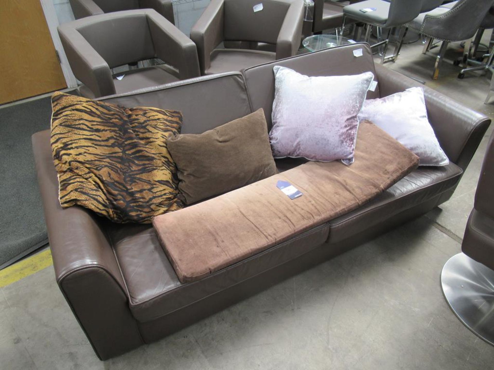 A brown leather effect two seater sofa with assorted cushions