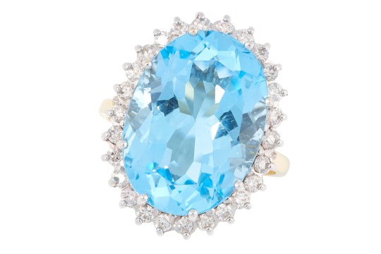 A TOPAZ AND DIAMOND CLUSTER RING in 18ct yellow gold, set with an oval cut topaz in a border of