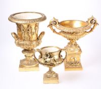 THREE GILT COMPOSITION URNS, each with twin handles. Largest 34cm high