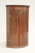 A GEORGE III MAHOGANY BOW-FRONT HANGING CORNER CUPBOARD