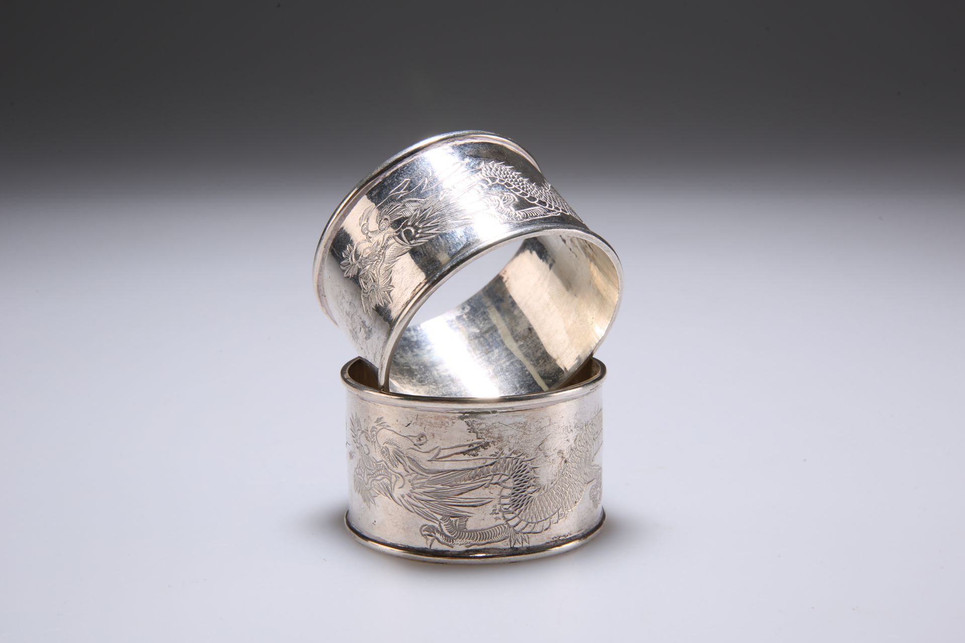 TWO CHINESE SILVER NAPKIN RINGS, of circular form, the central band engraved with a dragon, bears