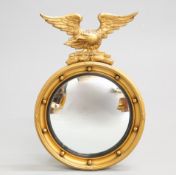 A REGENCY STYLE GILT-COMPOSITION CONVEX MIRROR, circular, with eagle crest. 56.5cm highThe absence