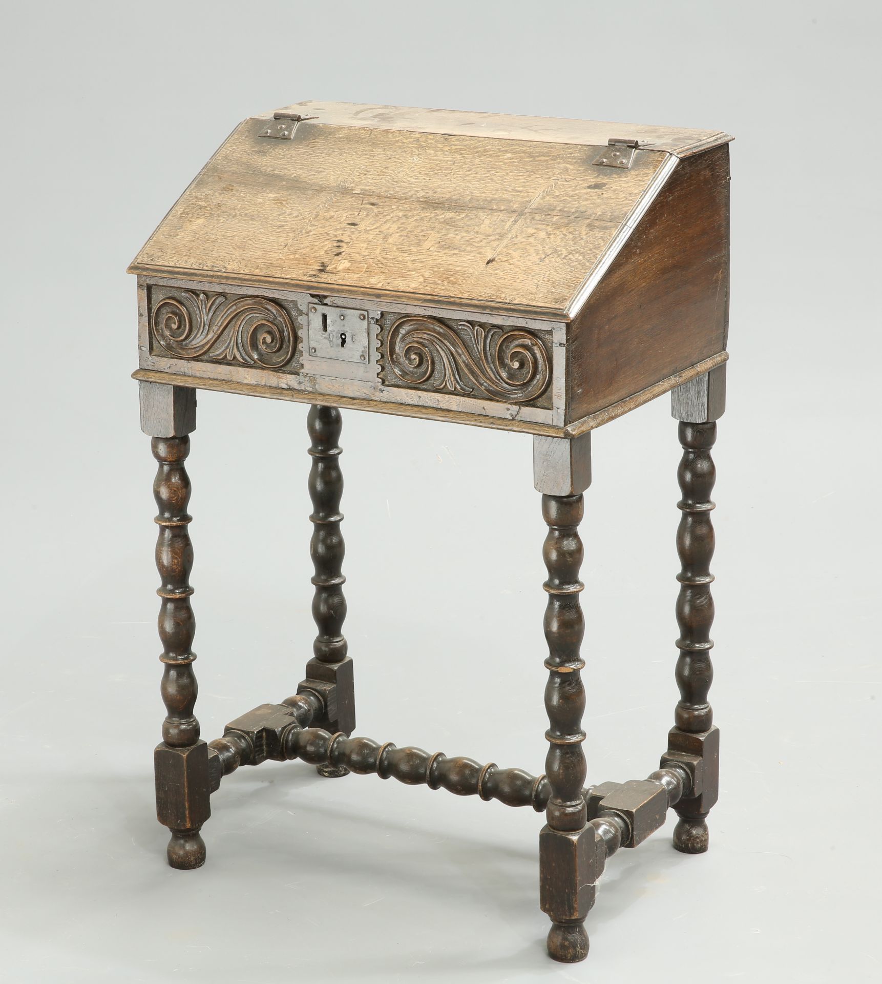 A 17TH CENTURY OAK BIBLE BOX, the slant-front box with scroll-carved front, now raised on a bobbin