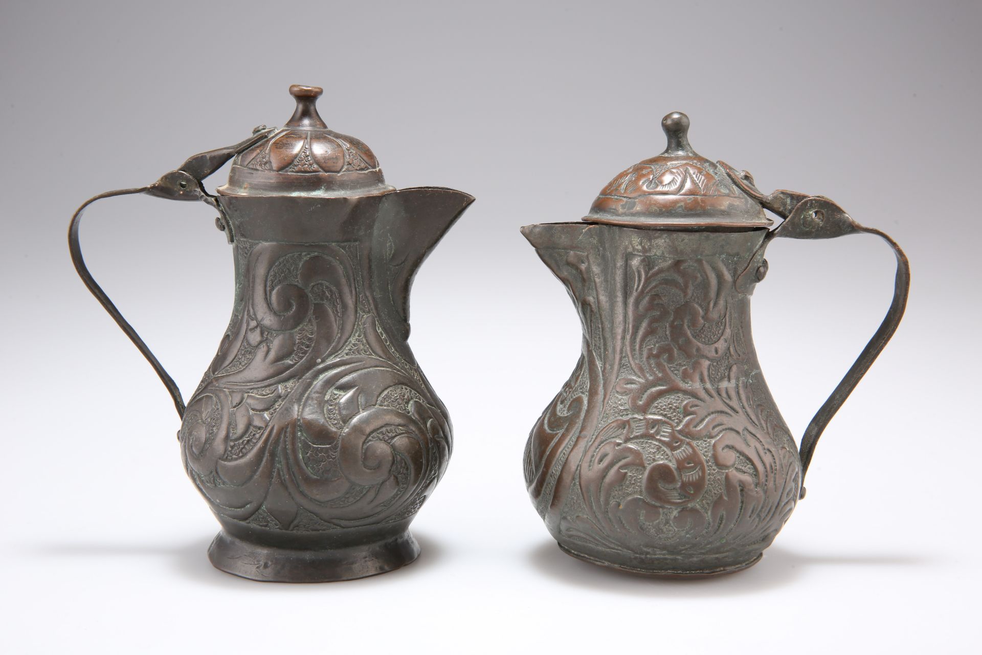 TWO 18TH CENTURY COPPER JUGS AND COVERS, each with hinged domed cover, repousse with scrolling