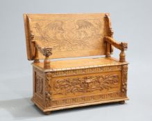 A LATE VICTORIAN CARVED OAK MONKS BENCH, with mask carved arms above a hinged box seat carved to the