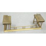 AN EDWARDIAN BRASS AND LEATHER CLUB FENDER, the pair of stools with green leather seats, raised on