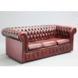 AN OX-BLOOD LEATHER THREE-SEATER CHESTERFIELD SOFA, with deep-buttoned back and arms, moving on