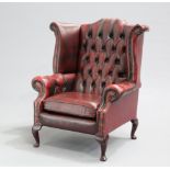 AN OX-BLOOD LEATHER CHESTERFIELD WING-BACK ARMCHAIR, with deep buttoned back and arms, raised on