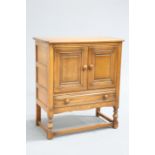 AN ERCOL GOLDEN DAWN SIDE CABINET, with a pair of cupboard doors over a long drawer, raised on block