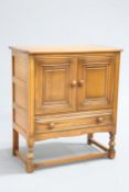 AN ERCOL GOLDEN DAWN SIDE CABINET, with a pair of cupboard doors over a long drawer, raised on block