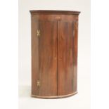 A GEORGE III MAHOGANY BOW-FRONT HANGING CORNER CUPBOARD