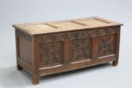 ~ A 17TH CENTURY OAK COFFER, with three panel lid above a rail carved with leaf-filled conjoined