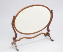 AN EDWARDIAN MAHOGANY OVAL DRESSING TABLE MIRROR, the large mirror plate swivelling between S-scroll